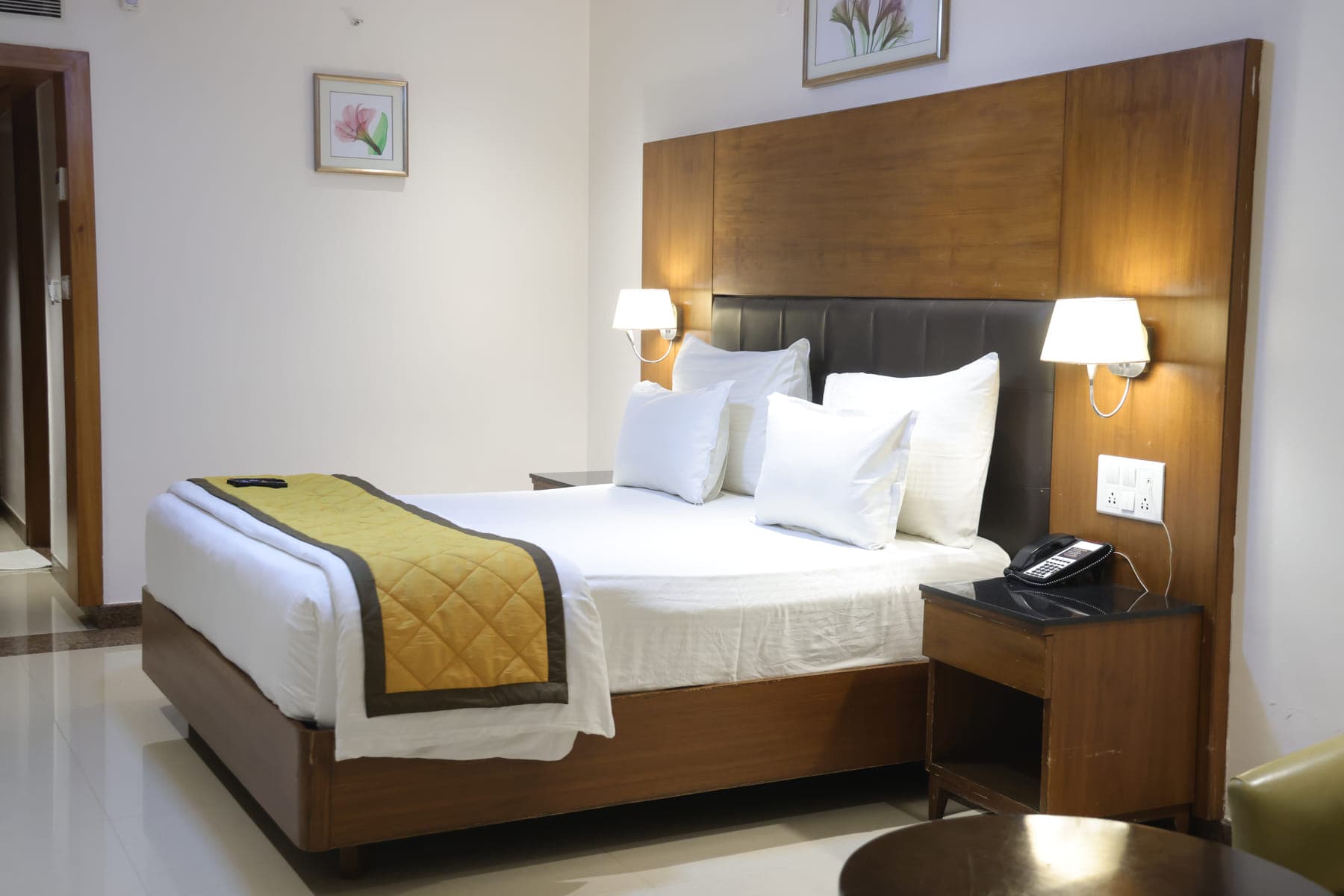 The bed in a Deluxe AC Room, made up with white linen and a gold runner