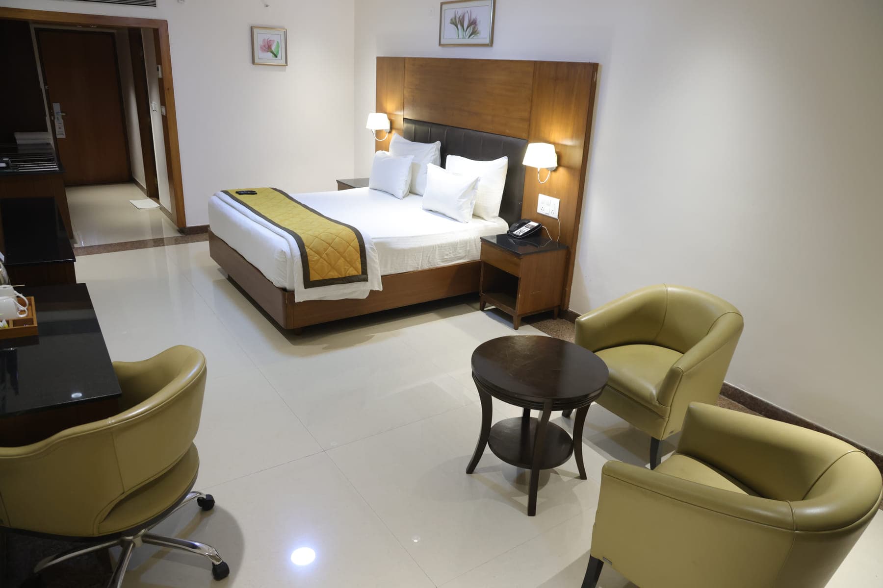 A Deluxe AC Room with a double bed, a work desk and two armchairs around a low table